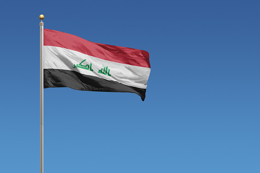Flag of Iraq in front of a clear blue sky