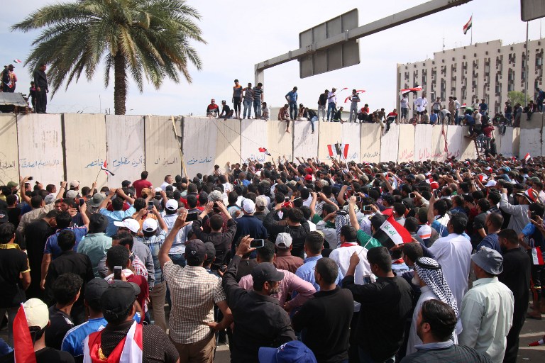 Iraqi protesters climb over a concrete wall surrounding the parliament (unseen) after breaking into Baghdad's heavily fortified "Green Zone" on April 30, 2016. 
Thousands of angry protesters broke into Baghdad's Green Zone and stormed the parliament building after lawmakers again failed to approve new ministers.
Jubilant supporters of cleric Moqtada al-Sadr invaded the main session hall, shouting slogans glorifying their leader and claiming that they had rooted out corruption. / AFP PHOTO / HAIDAR MOHAMMED ALI